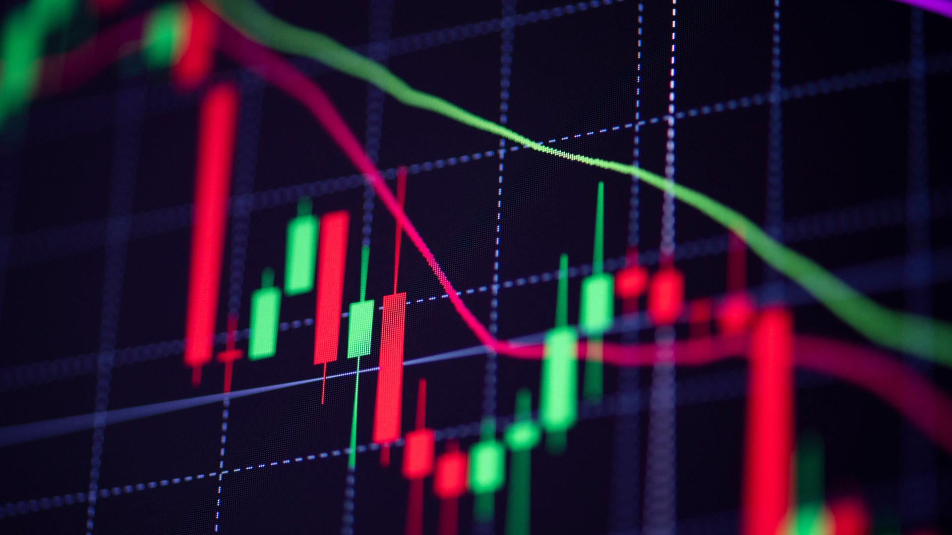 Extreme close-up of a dark trading screen showing overlapping red and green candlestick bars beneath blurred green and pink moving-average lines crossing a faint blue grid.